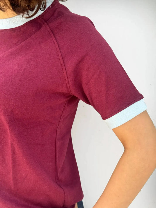 Woman wearing a burgundy / maroon t-shirt with sky blue trim against a plain background
