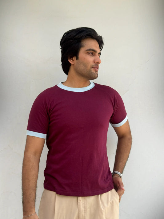 Man wearing a burgundy / maroon t-shirt with sky blue trim against a plain background