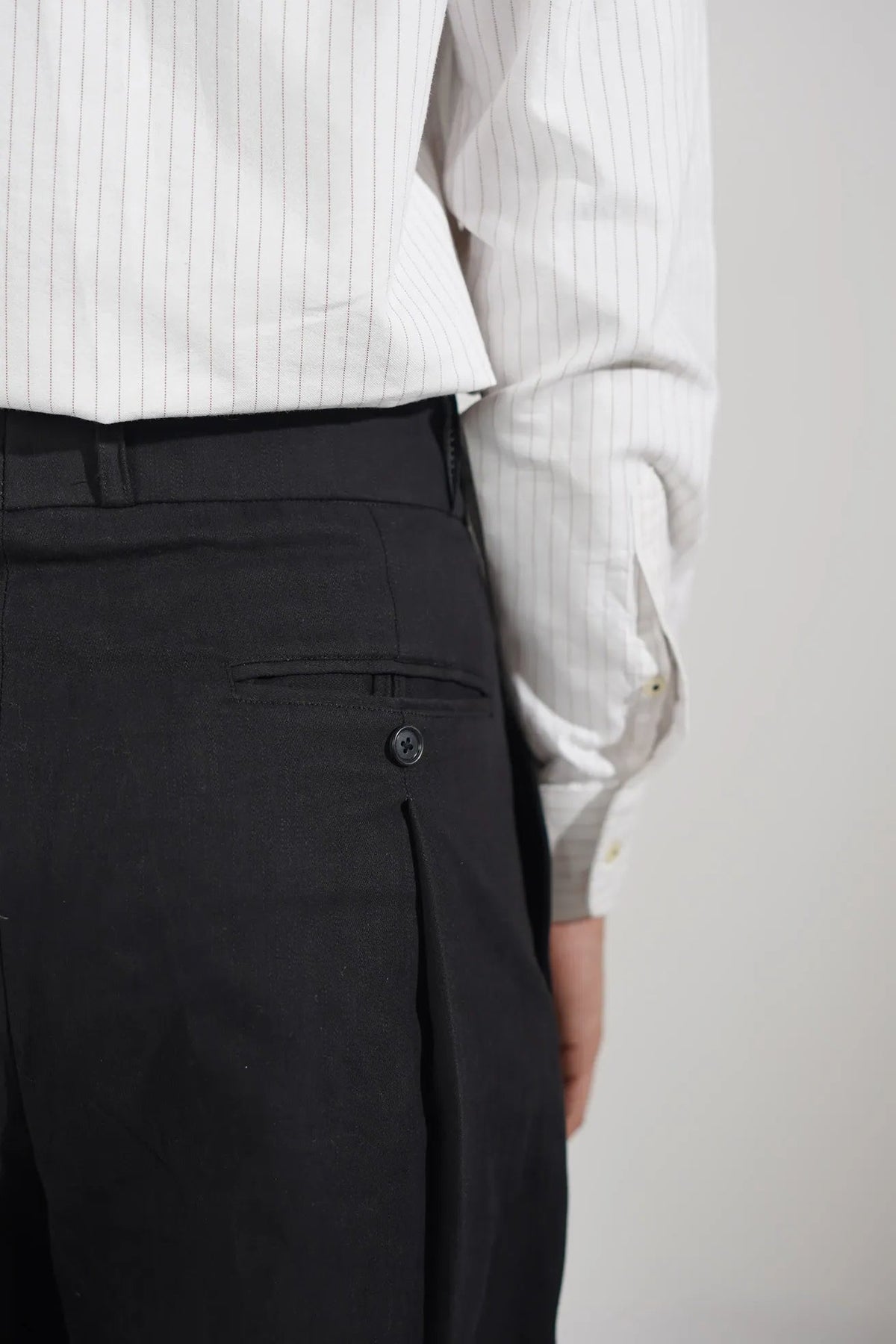 Close-up of a person wearing black trousers and a white pinstriped dress shirt, cropped to show the waist area and hands holding the shirt.