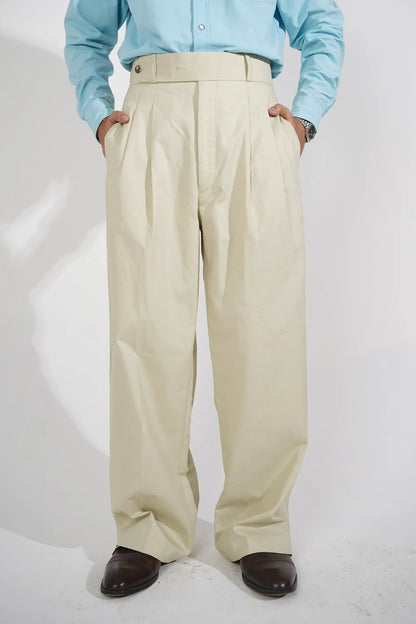 A person wearing beige wide-leg pleated trousers, a light blue long-sleeve button-up shirt, and dark brown leather shoes, photographed from a high angle against a white studio background.