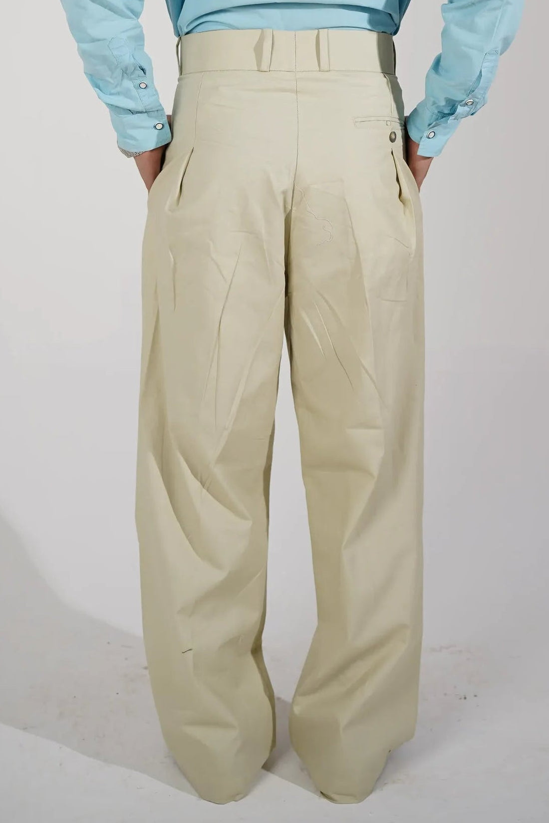 A person viewed from above wearing a light blue long-sleeve shirt and cream-colored trousers, standing against a plain light gray studio background.