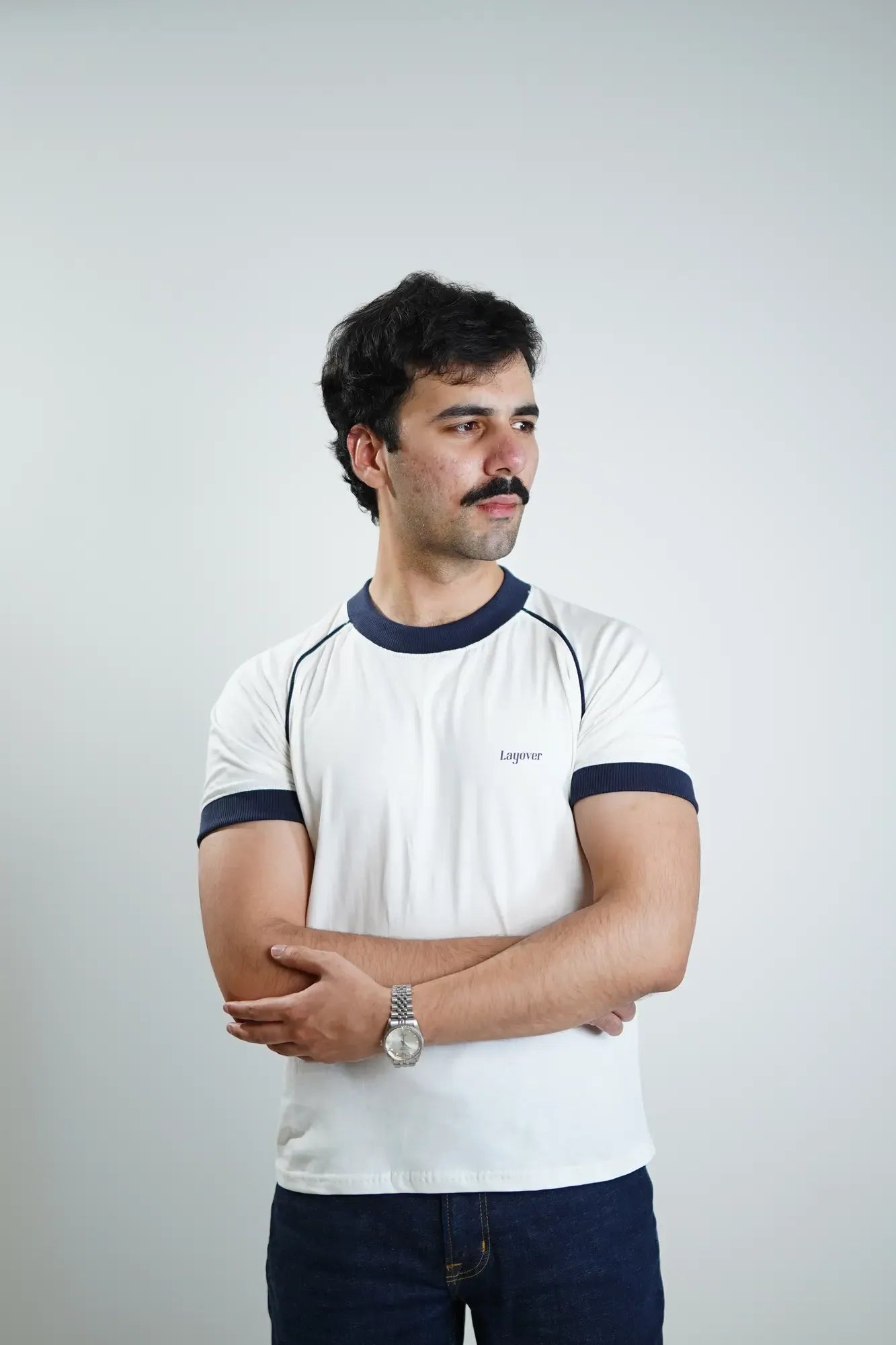 Man wearing a white t-shirt with navy accents and 'Layover' text on a plain background
