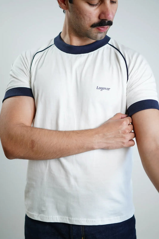 Man wearing a white t-shirt with navy accents and 'Layover' branding on a plain background