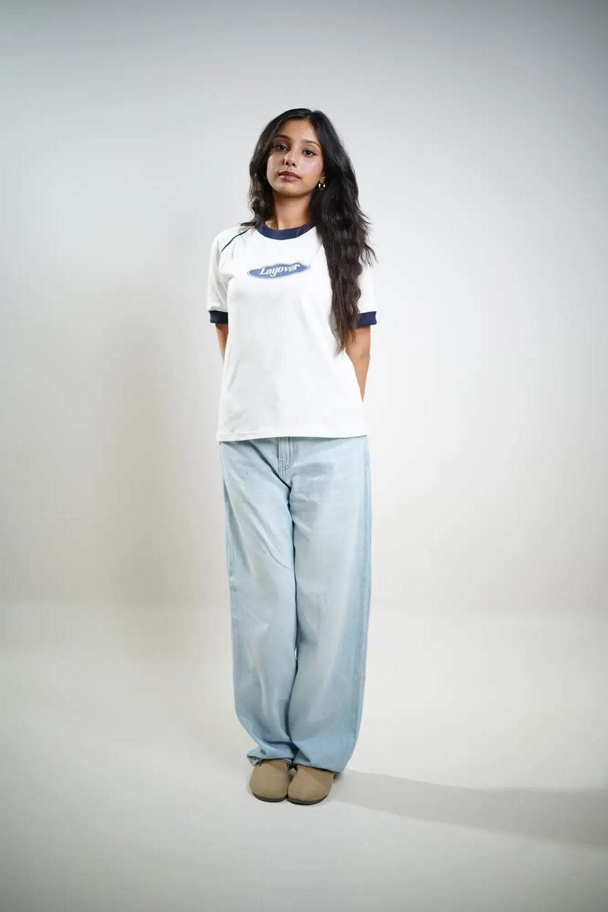 Woman wearing a white t-shirt with blue trim and light blue jeans on a plain background