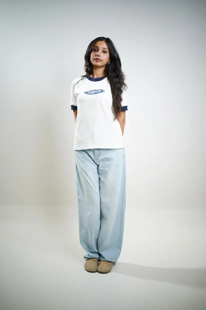 Woman wearing a white t-shirt with blue trim and light blue jeans on a plain background