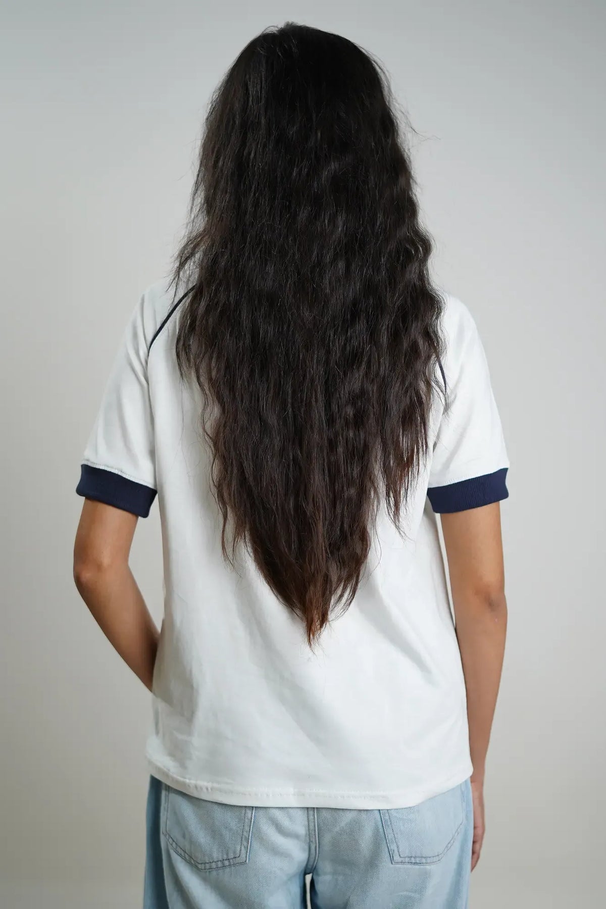 Woman wearing a white t-shirt with navy trim and light blue jeans on a plain background