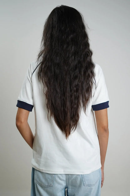 Woman wearing a white t-shirt with navy trim and light blue jeans on a plain background