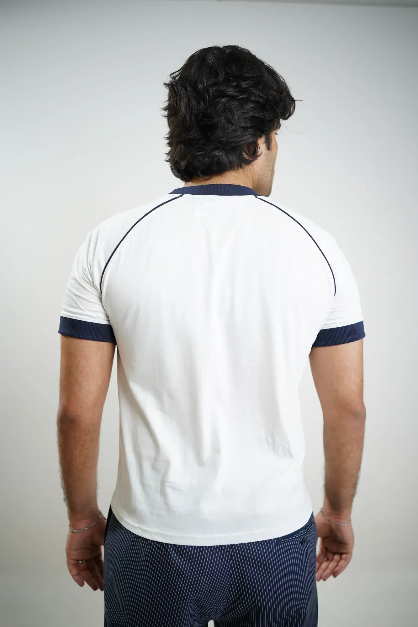 Man wearing a white t-shirt with navy accents on a plain background. Raglan sleeves with piping