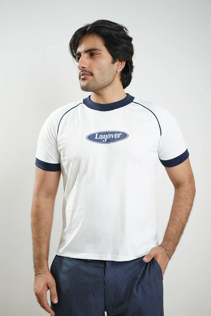 Man wearing a white t-shirt with blue accents and a logo, standing against a plain background with Layover logo on chest