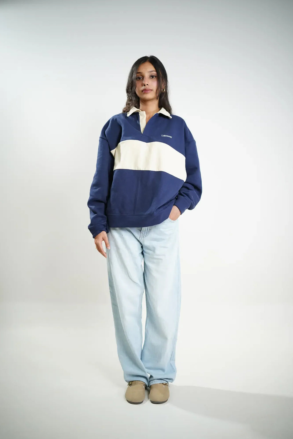 Person wearing a blue and beige rugby shirt with light blue pants on a white background
