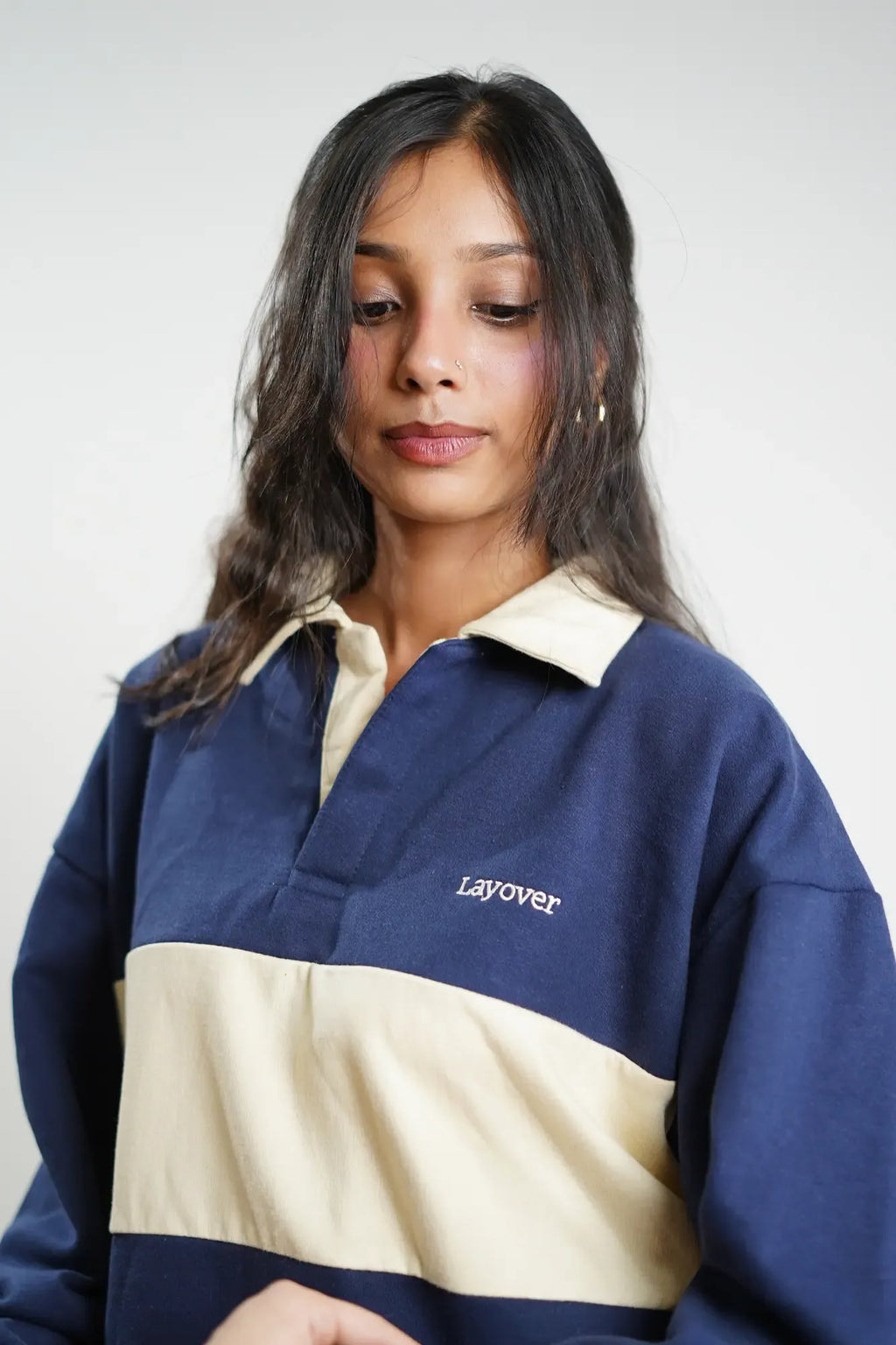 Woman wearing a blue and beige pullover with 'Layover' branding on a white background