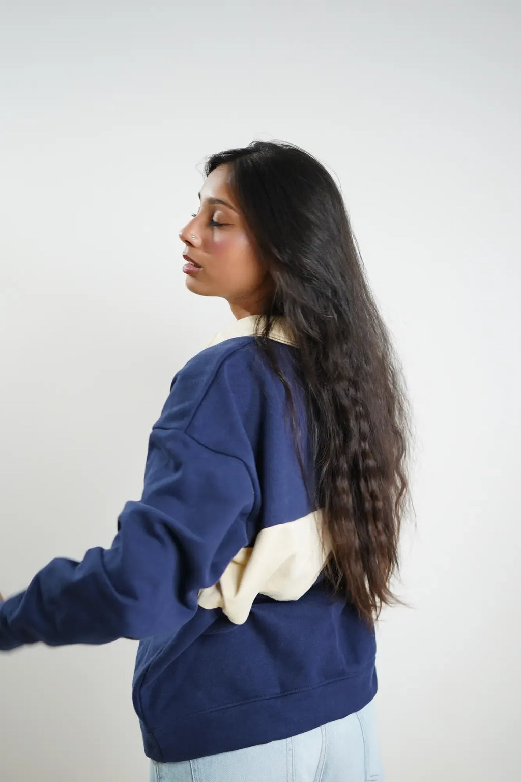 Woman wearing a blue sweatshirt with a beige design on a plain background