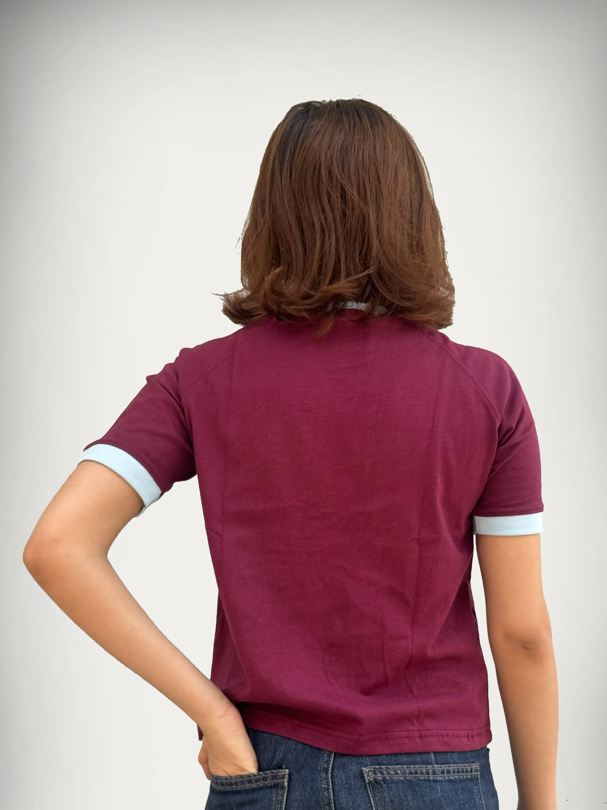 Woman wearing a burgundy / maroon t-shirt with sky blue trim against a plain background