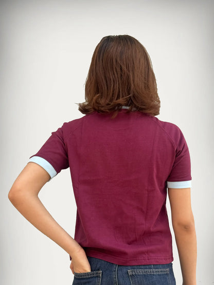 Woman wearing a burgundy / maroon t-shirt with sky blue trim against a plain background
