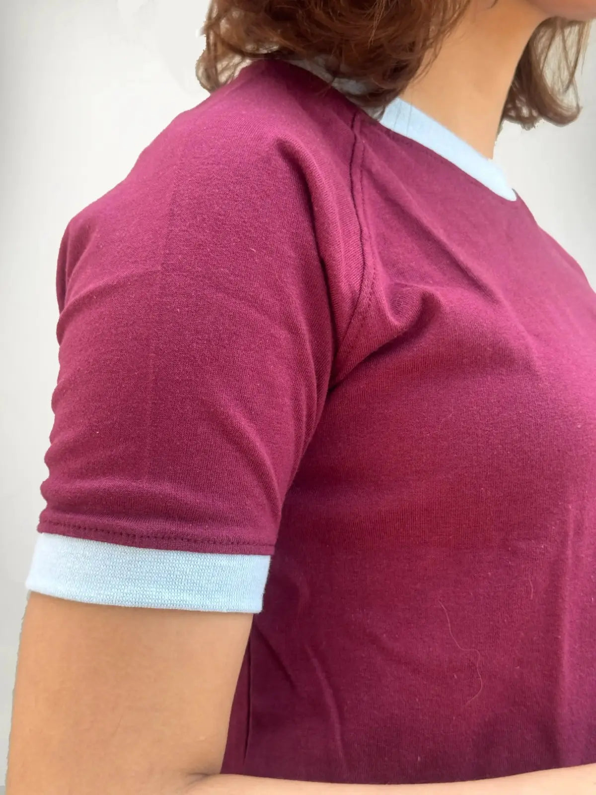 Close-up of a person wearing a maroon shirt with light blue trim on a white background