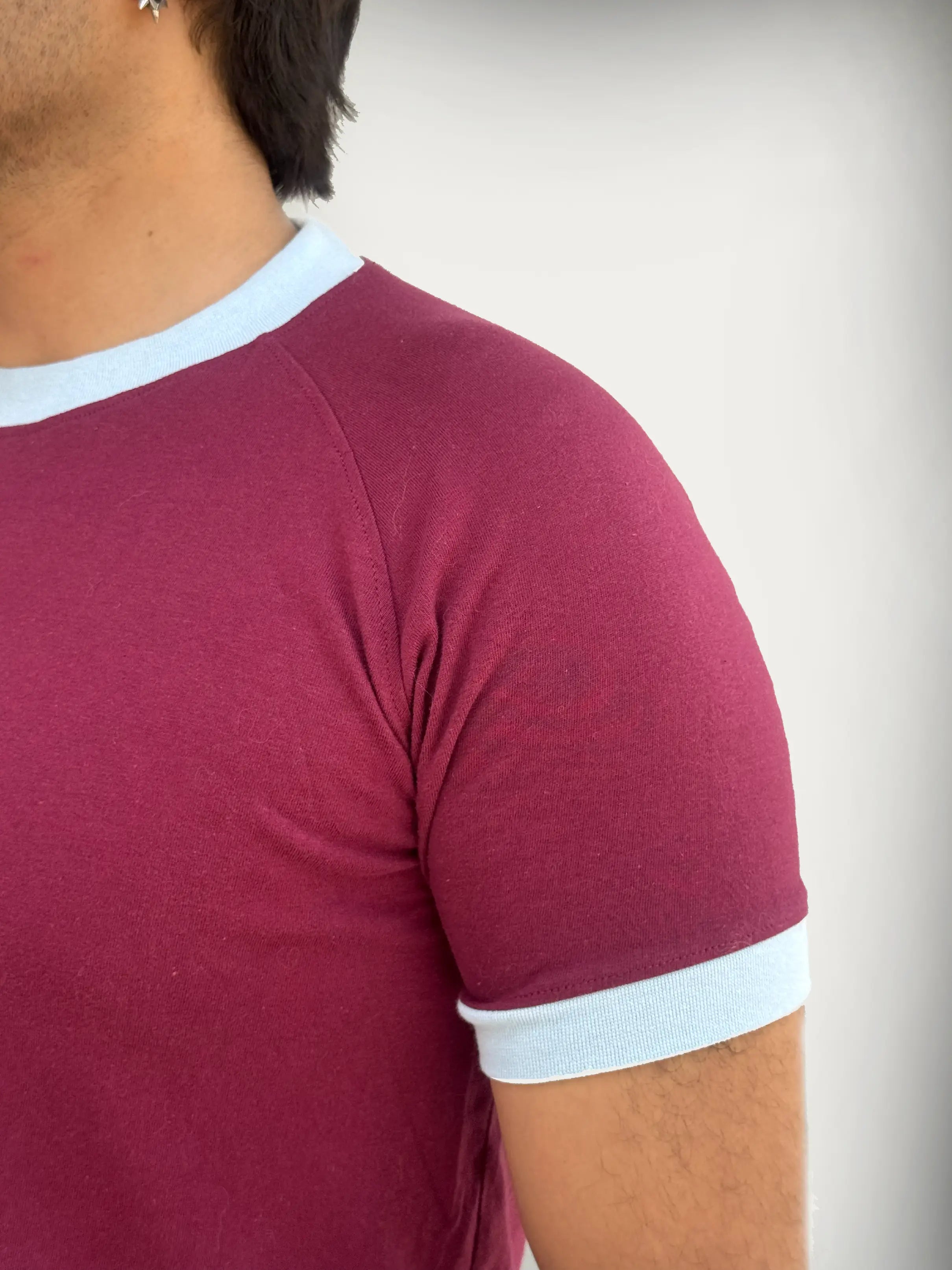 Man wearing a burgundy / maroon t-shirt with sky blue trim against a plain background