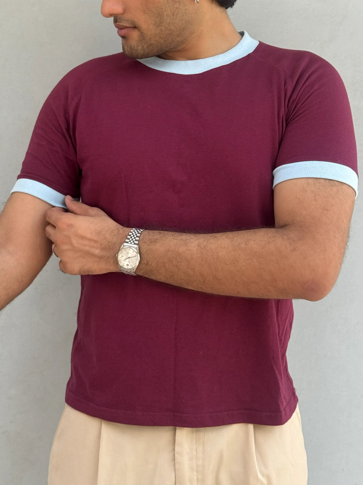 Man wearing a burgundy / maroon t-shirt with sky bluetrim against a plain background